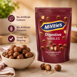 McVities Digestive Nibbles milk chocolate biscuit balls in a dark red stand-up pouch, shown next to a bowl of the chocolate balls and a few loose pieces on a tabletop. Three callout icons on the left read 'No Artificial Colours', 'No Artificial Flavours', and 'Great for Sharing'.