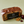 A packaged loaf of fruit cake on a light sage green background, with a few whole walnuts and dried cherries placed beside it. The cake is wrapped in clear plastic and has a black label reading 'The Original Cake Co.