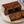 A loaf of Rich Sultana Fruit Cake by The Orchard Cake Co. in clear plastic packaging with a black label, displayed on a white plate with two sliced pieces showing the dense fruit and dried fruit texture.