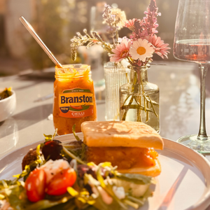 Burger with Branston pickle on a plate with flowers and a glass in the background
