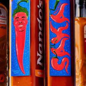Close-up of Nando's hot sauce bottles showing colorful labels with illustrated red chili peppers and the Nando's branding, with amber-orange sauce visible in the bottles.