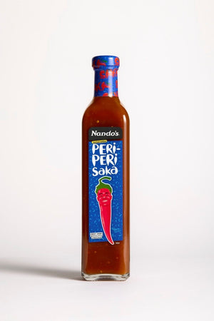A bottle of Nando's Peri-Peri Saka chili sauce, featuring a clear glass bottle filled with reddish-brown sauce and a blue label with a red chili pepper illustration, set against a plain white background.