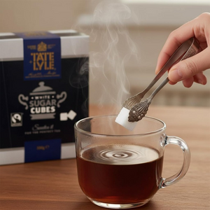 Person adding Tate & Lyle white sugar cube to a steaming cup of tea with Tate & Lyle sugar cubes packaging in the background.
