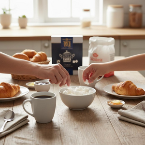 Two people preparing a breakfast scene with croissants, coffee, and a bowl of sugar on a wooden table.