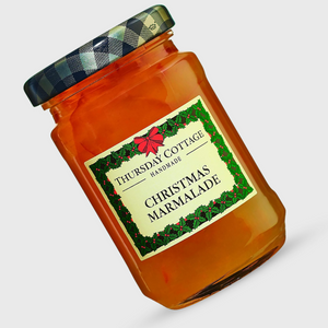 A glass jar of Thursday Cottage Handmade Christmas Marmalade, filled with amber-colored marmalade and featuring a green and black plaid lid, set against a light gray background.