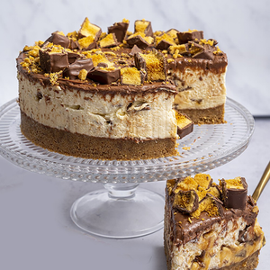 Layered dessert with chocolate and peanut butter chunks on a glass cake stand.
