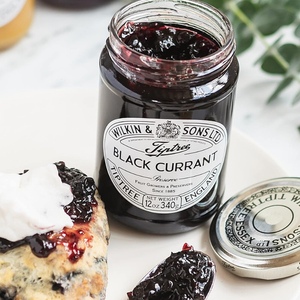 Jar of black currant preserve with a cake and jam on a white surface