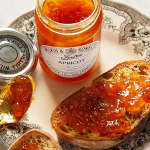 Jar of apricot jam with a spoonful on a piece of bread, on a decorative plate.