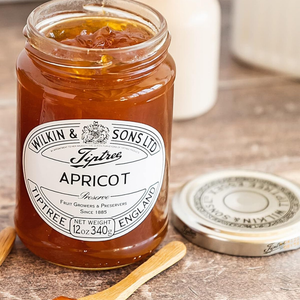 Jar of Tiptree Apricot Preserve with a wooden spoon on a wooden surface
