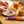 Person holding a Violet Crumble bar with a plate of brownies, iced tea, and peanut butter on a wooden table.