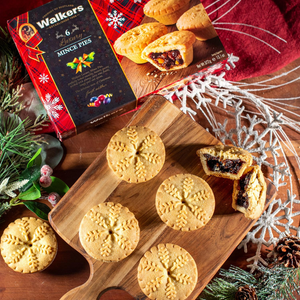 Walkers mince pies on a wooden board with a box of mince pies in the background.