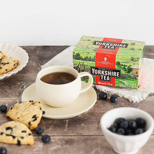Yorkshire Tea box with a cup of tea, cookies, and blueberries on a wooden table.