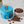 A blue Paddington bear metal tin filled with chocolate discs, shown beside a white bowl of more chocolates and scattered chocolate pieces on a light marble surface.
